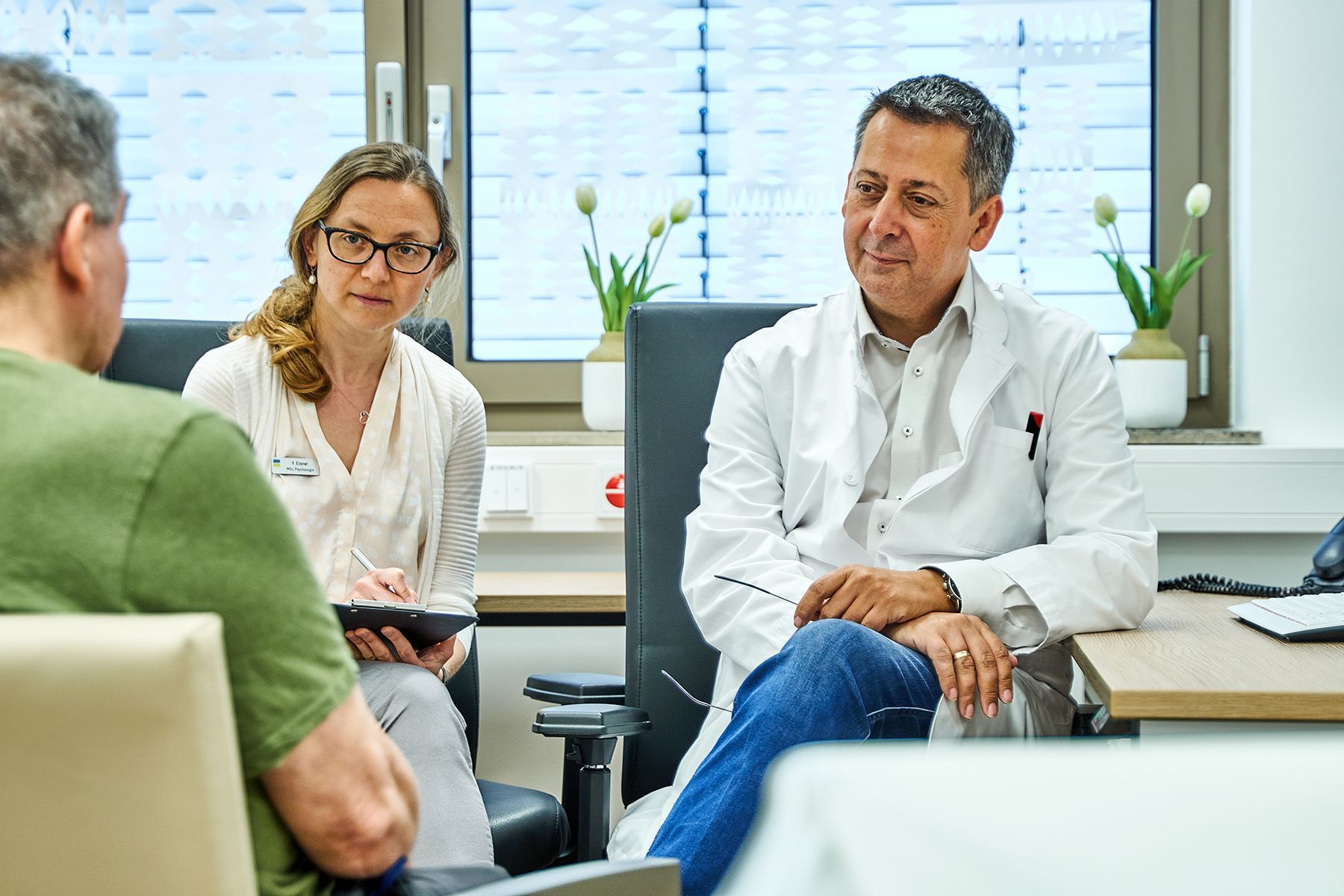 Eine Psychologin und ein Arzt im Gespräch mit einem Patienten.