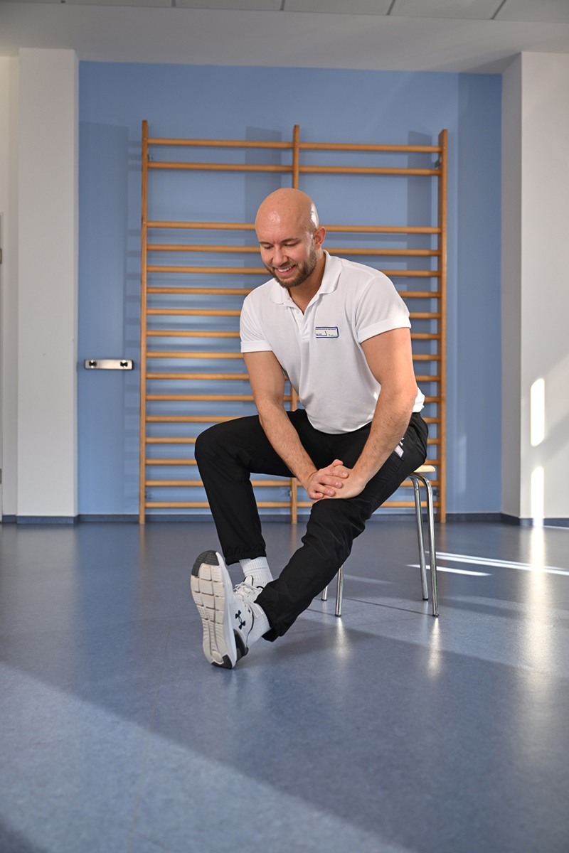 Ein Mann sitzt auf einem Stuhl und macht eine Übung vor